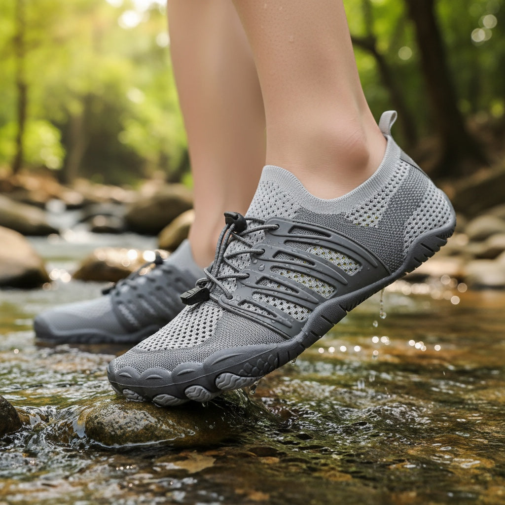 Person wearing gray barefoot water shoes while walking through a shallow outdoor stream